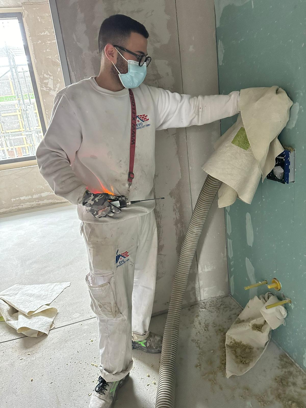 Gipser mit Ausflockungsschlauch an einer Trockenbauwand