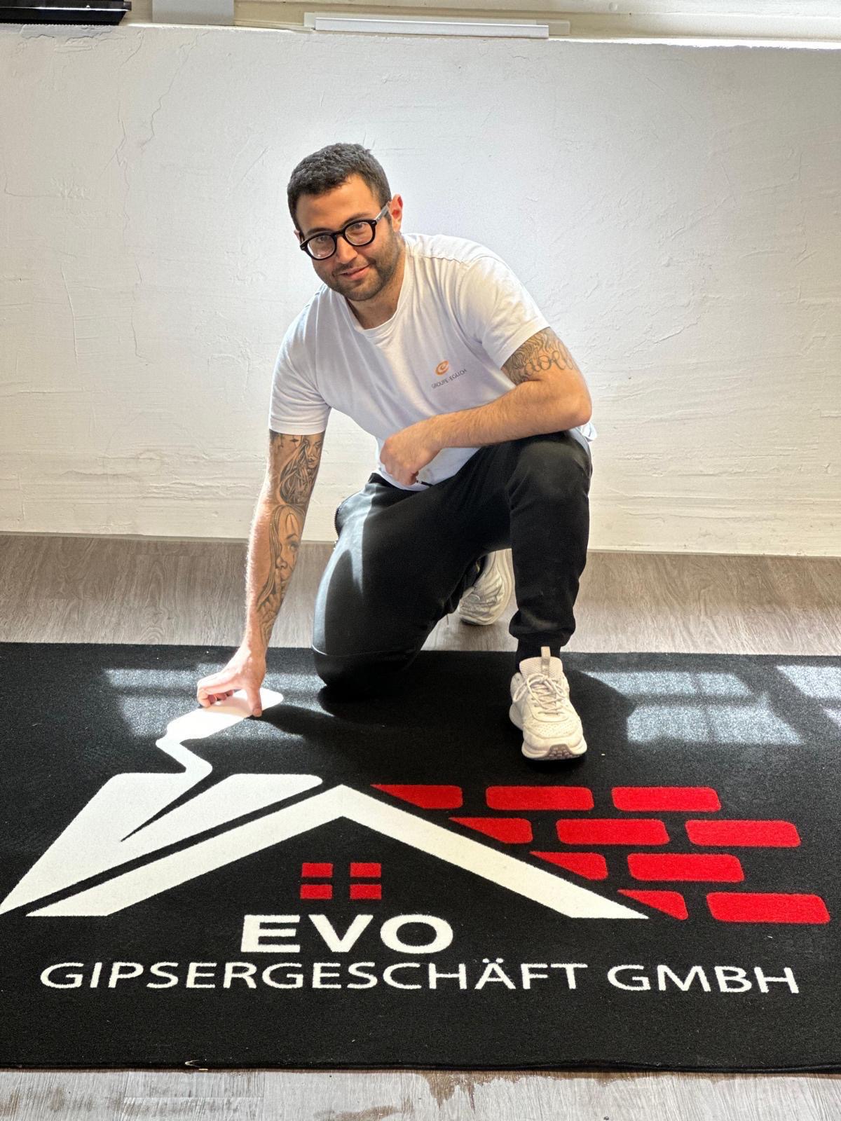Enrico Paolisso kniet auf einer Fussmatte mit dem Logo von Evo Gipsergeschäft